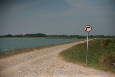 Road sign by stream against sky