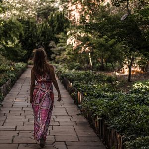 Rear view of woman walking on footpath amidst trees