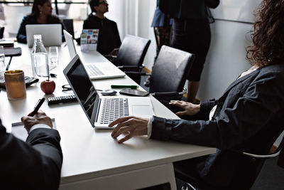 Business people sitting at conference table by female colleagues standing in board room during meeting