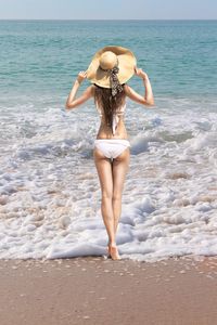 Rear view of young woman in bikini standing on beach