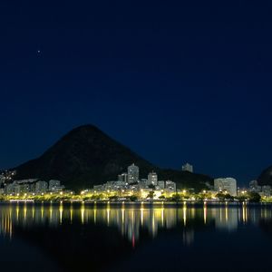 Illuminated city by lake against clear blue sky at night