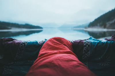 Person wrapped in blanket by lake against sky