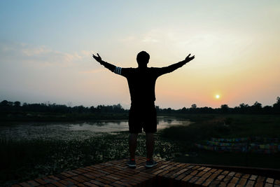 Rear view of silhouette man standing at shore against sky