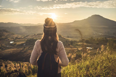 Rear view of woman standing on mountain against sky during sunset