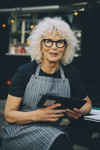 Portrait of senior owner with digital tablet against food truck in city