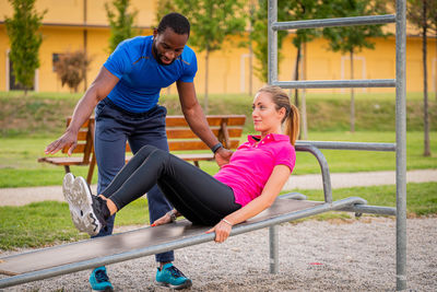 Afro american 
instructor coaching helping woman doing push-ups on cross fit horizontal bar station