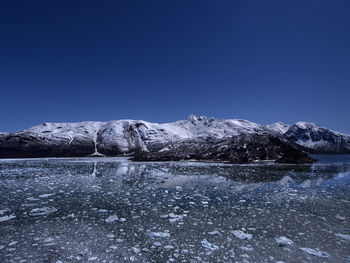 Snow floating on river by mountain against clear blue sky