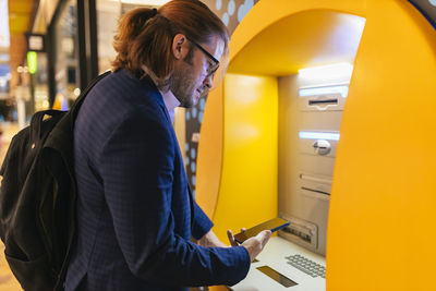 Businessman using mobile phone at subway ticket machine