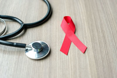 High angle view of stethoscope and red ribbon on wooden table