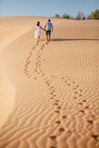 Rear view of couple walking on sand at desert