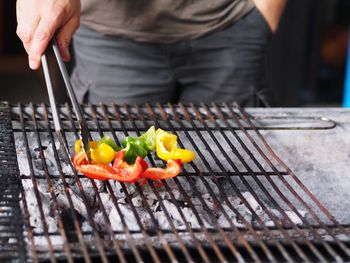 Close-up of man preparing bell peppers on barbecue grill