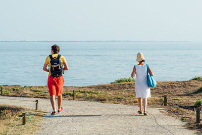 Rear view of man and woman walking on footpath leading towards sea