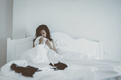 Terrified woman sitting on bed with bra in foreground