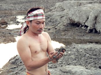 Shirtless man standing on rock by pond