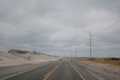 Car on road by landscape against cloudy sky