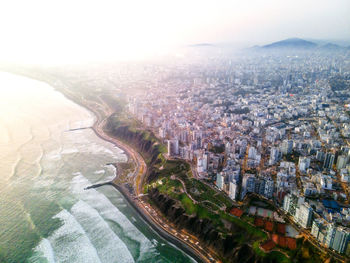 Breathtaking aerial view of wavy ocean washing sandy coastline near modern residential and commercial building against cloudy blue sky in lima