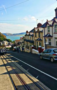 Vehicles on road by sea against sky in city