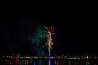 Firework display over illuminated cityscape against sky at night