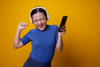 Young woman using smart phone against yellow background