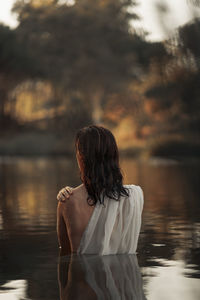 Rear view of woman standing by lake against sky during sunset