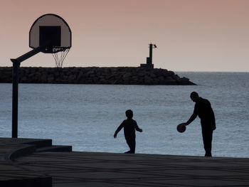 Silhouette of people by sea against sky during sunset