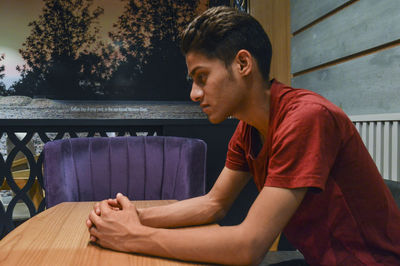 Side view of young man sitting on table