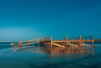 Pier over sea against clear blue sky