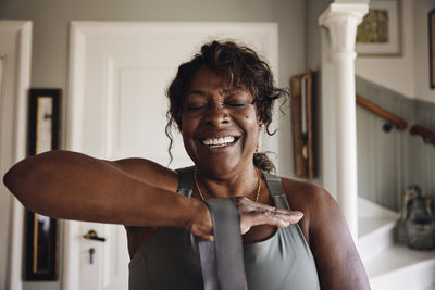 Happy mature woman with eyes closed stretching resistance band while exercising at home