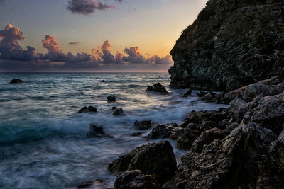 Rocks in sea against sky during sunset