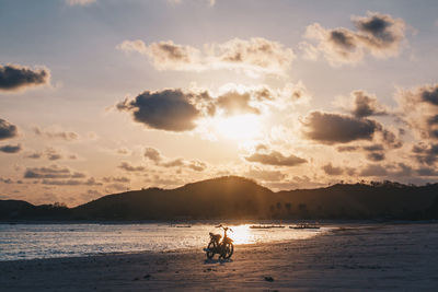 People sitting on beach against sky during sunset