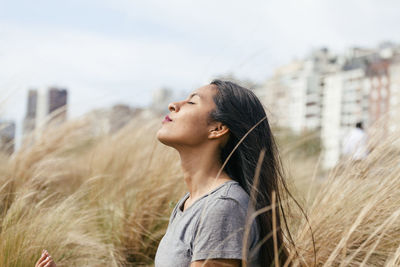 Side view of young woman looking away against sky