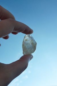 Close-up of hand holding ice cream against blue sky