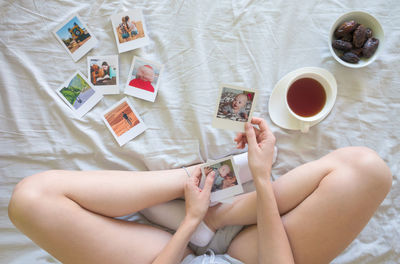 Low section of young woman holding photographs while sitting on bed