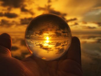 Close-up of hand holding crystal ball against sunset sky