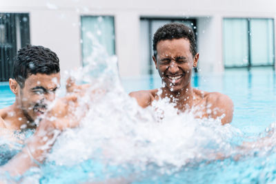 Man smiling with his eyes closed as he splashes around playing with his friends in the water of a pool