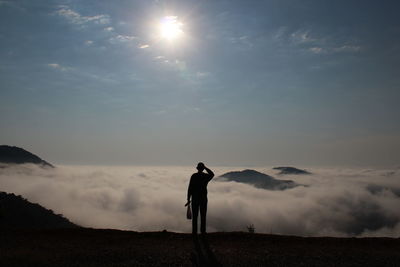 Rear view of silhouette man standing on landscape against sky at sunset