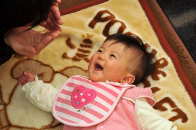 High angle view of woman playing with cute baby girl lying on blanket at home