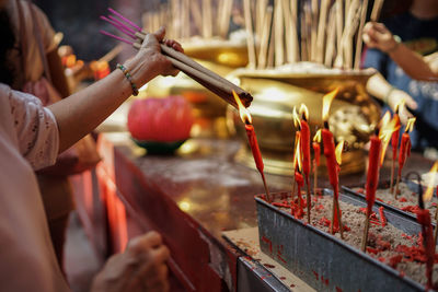 Cropped image of woman burning incense sticks at altar