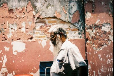 Side view of mature man standing by damaged wall