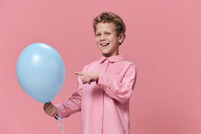 Portrait of smiling young woman with balloons against pink background