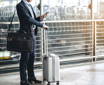 Low section of businessman with luggage using smart phone while standing on footbridge