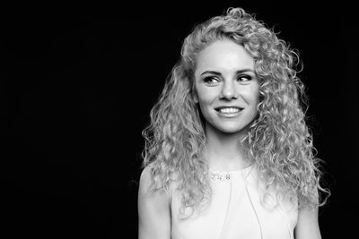 Smiling woman with curly hair standing against black background
