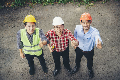 Portrait of engineers gesturing thumbs up sign while standing on road