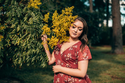 Portrait of smiling young woman standing by flowering plants