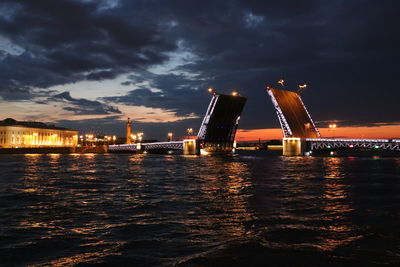 Illuminated city by sea against sky at night