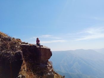 Man sitting on rock by mountains against sky