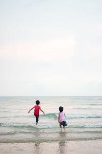 Siblings playing on shore at beach against sky