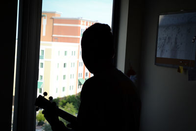 Rear view of silhouette man standing by window in building