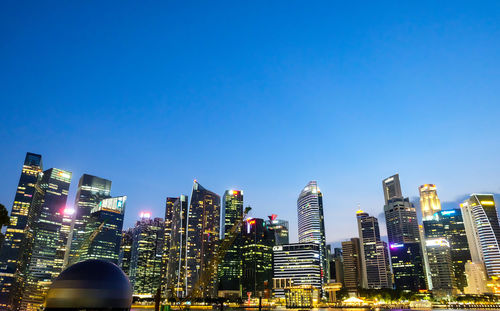 Illuminated buildings in city against clear blue sky