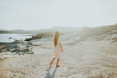 Rear view of woman walking on beach against sky